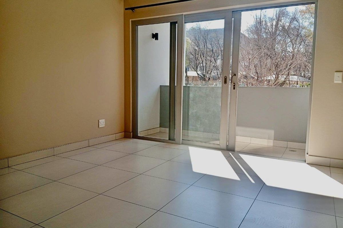 A bright, empty living area featuring neutral tiled flooring and large sliding glass doors that provide direct access to a private balcony.