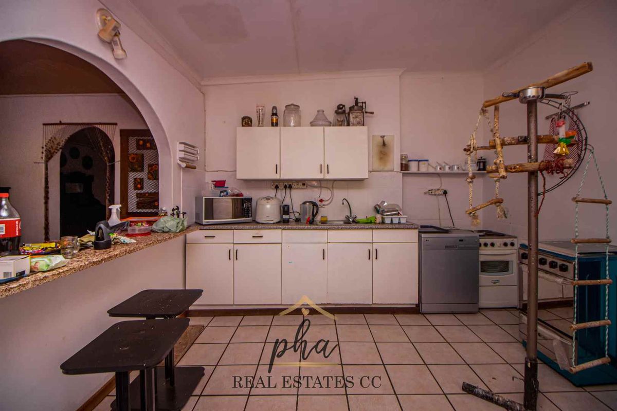 A functional kitchen area featuring white cabinetry, a granite-look countertop, and tiled flooring, opening into an adjacent living space.