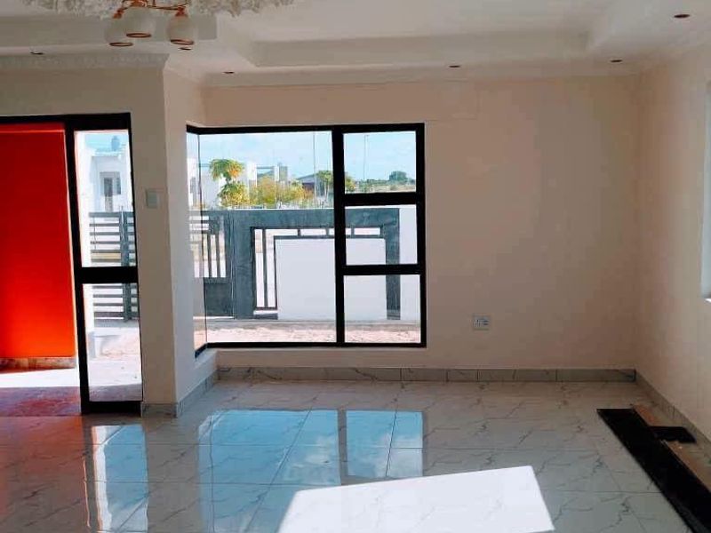Bright and spacious living area featuring modern porcelain tile flooring, a decorative recessed ceiling, and large aluminium-framed windows providing ample natural light.