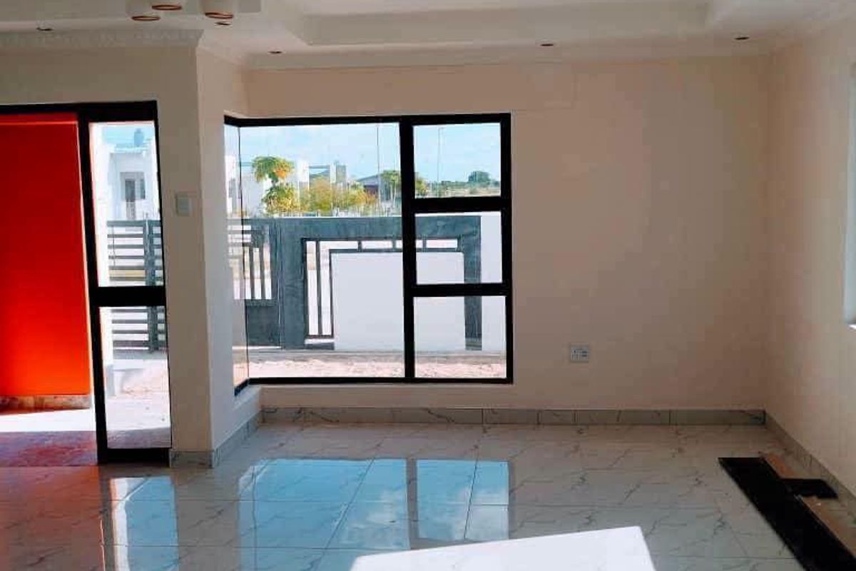 Bright and spacious living area featuring modern porcelain tile flooring, a decorative recessed ceiling, and large aluminium-framed windows providing ample natural light.
