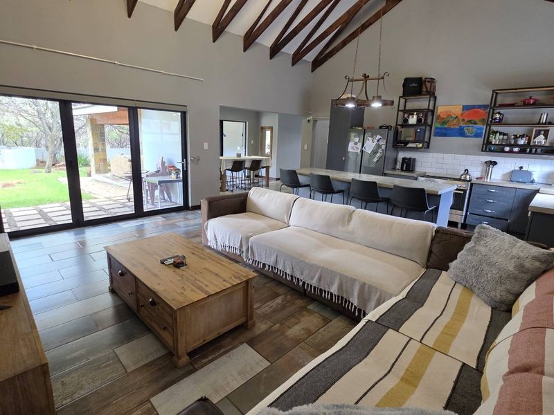 Spacious open-plan living area featuring vaulted ceilings with exposed timber beams, a modern kitchen with island, and large sliding doors leading to the patio.