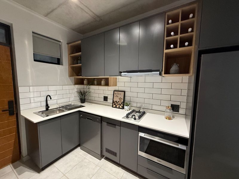 Modern kitchen featuring sleek grey cabinetry, white subway tile backsplash, stone countertops, integrated appliances, and an exposed concrete ceiling.