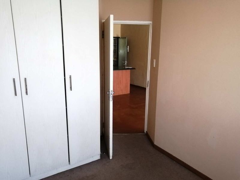 A vacant bedroom featuring built-in wardrobes and carpeted flooring, with a doorway leading to an adjacent living area.