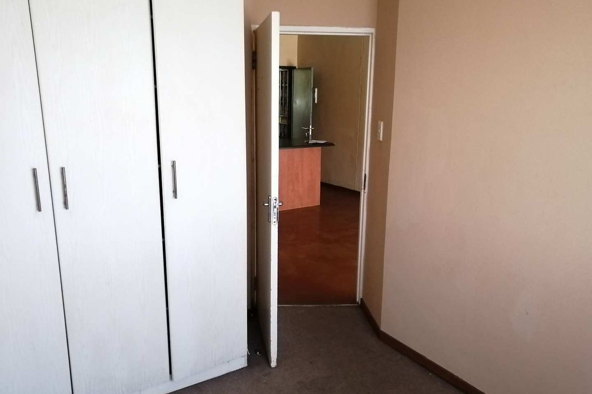 A vacant bedroom featuring built-in wardrobes and carpeted flooring, with a doorway leading to an adjacent living area.