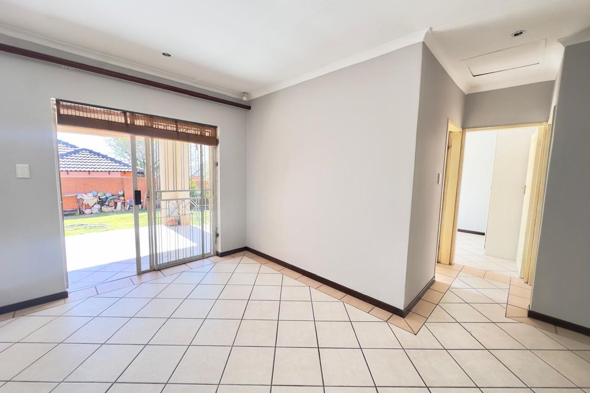 An empty, well-lit living area featuring neutral tiled flooring, coved ceilings, and a sliding glass door providing direct access to the rear patio.