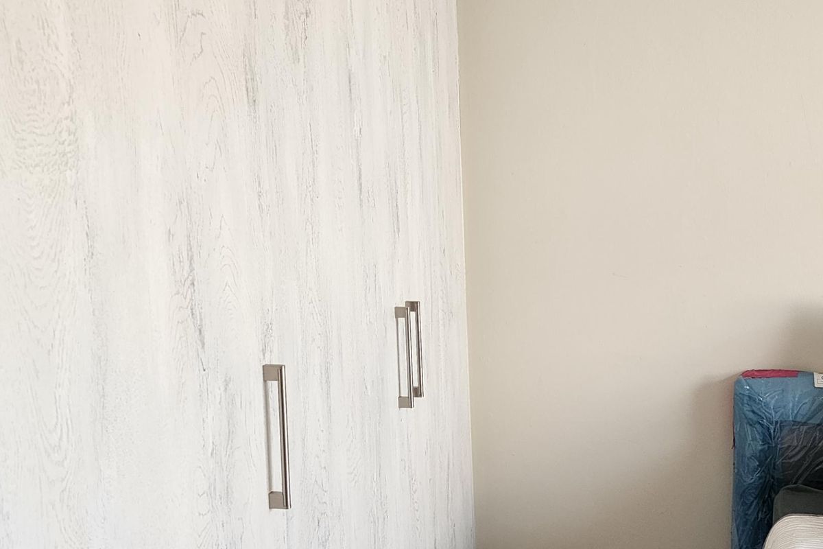 A bedroom featuring built-in wardrobes with a light wood-grain finish and modern metal handles.