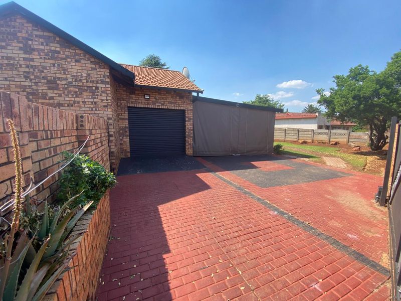 Front exterior view of the property featuring a brick facade, paved driveway, single garage, and an attached carport structure.