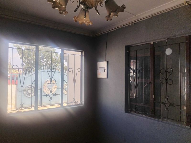 An empty living area featuring dark painted walls, security bars on windows, and an existing electrical distribution board.