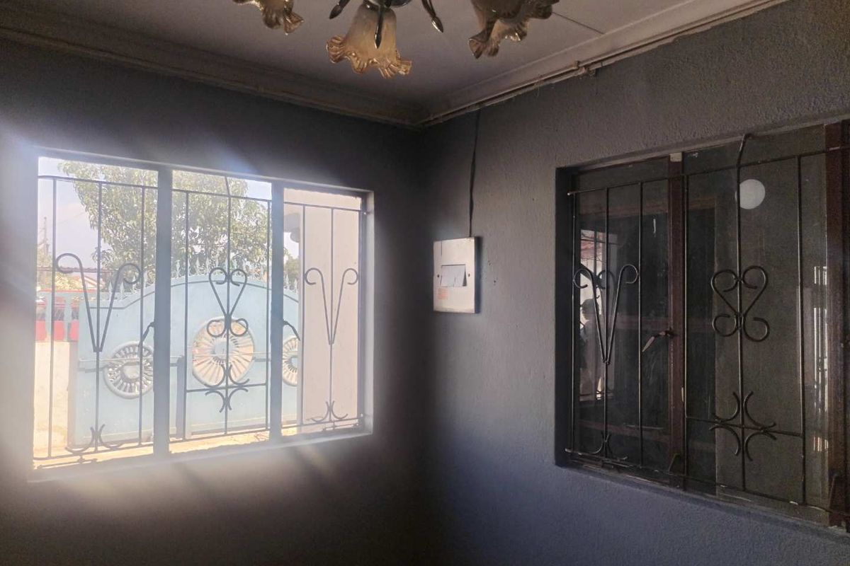 An empty living area featuring dark painted walls, security bars on windows, and an existing electrical distribution board.