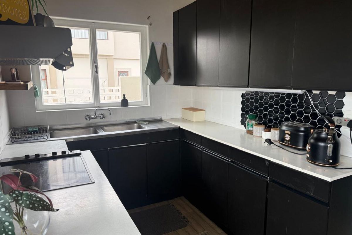 A functional kitchen featuring black cabinetry, white countertops, a double basin sink, and a modern hexagonal tile backsplash.