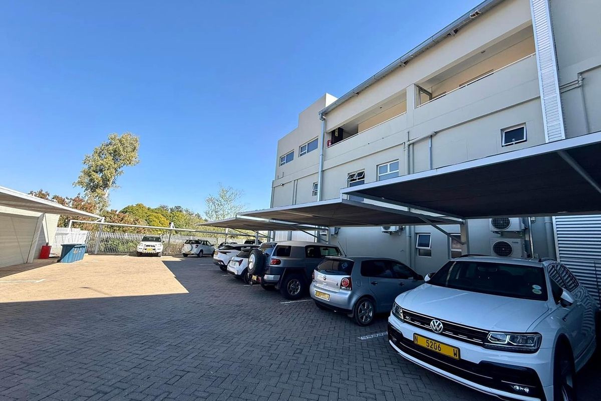 Rear exterior view of the office building featuring a paved parking area with covered carports and external air conditioning units.