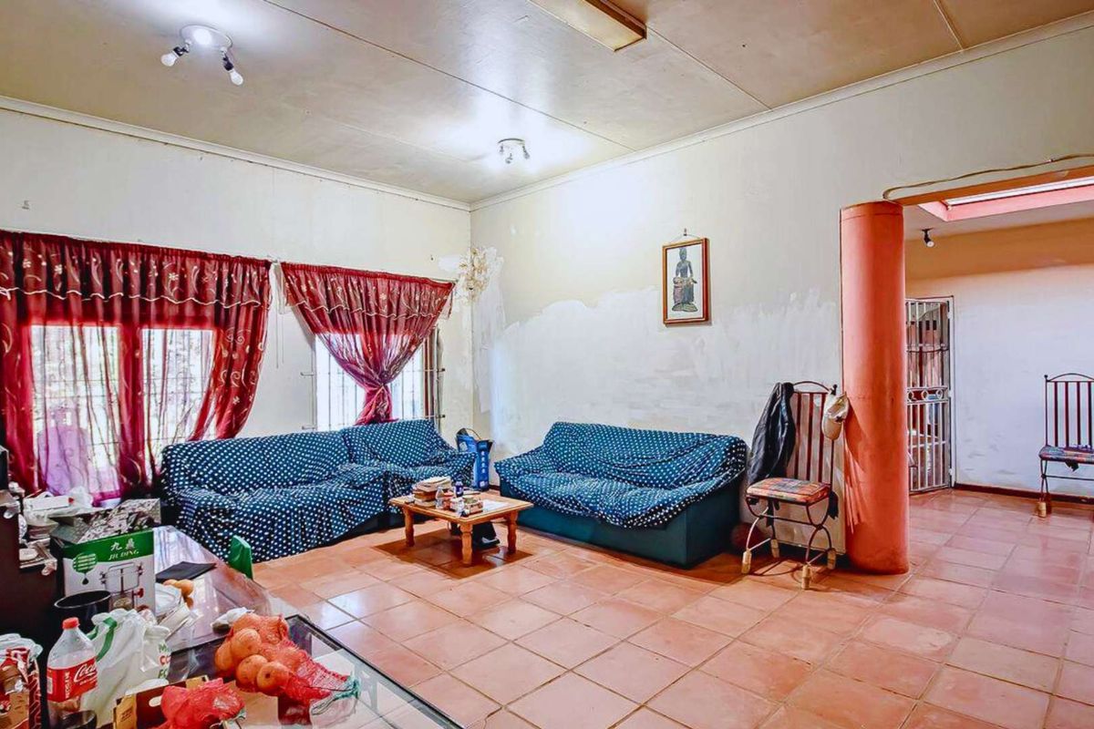 A spacious living area featuring terracotta floor tiles, a structural pillar, and large windows with security bars.