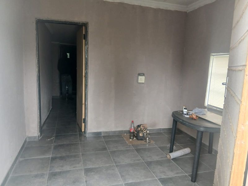 An unfinished living area featuring grey tiled flooring and raw plaster walls, offering a blank canvas for renovation and interior design.