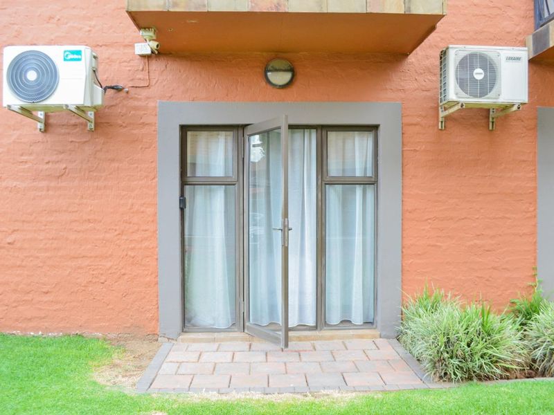 Rear exterior view of an apartment featuring a paved patio, aluminium glass door, and two wall-mounted air conditioning condenser units.