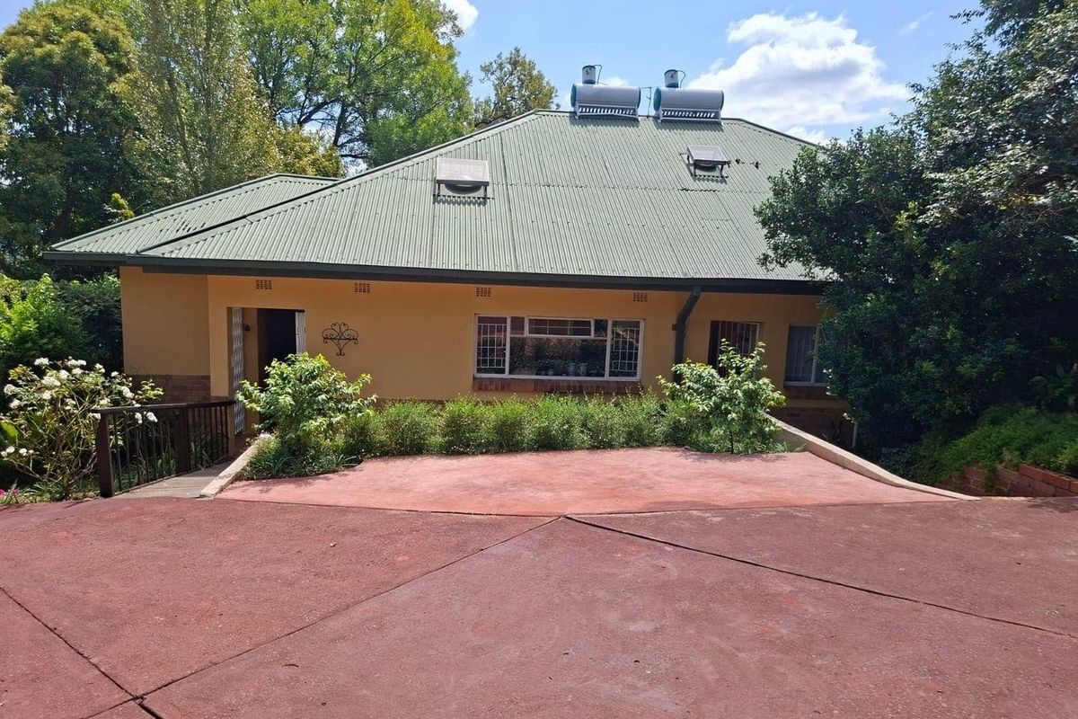 Rear view of the house featuring a corrugated metal roof with solar geysers, a paved patio area, and established garden surroundings.