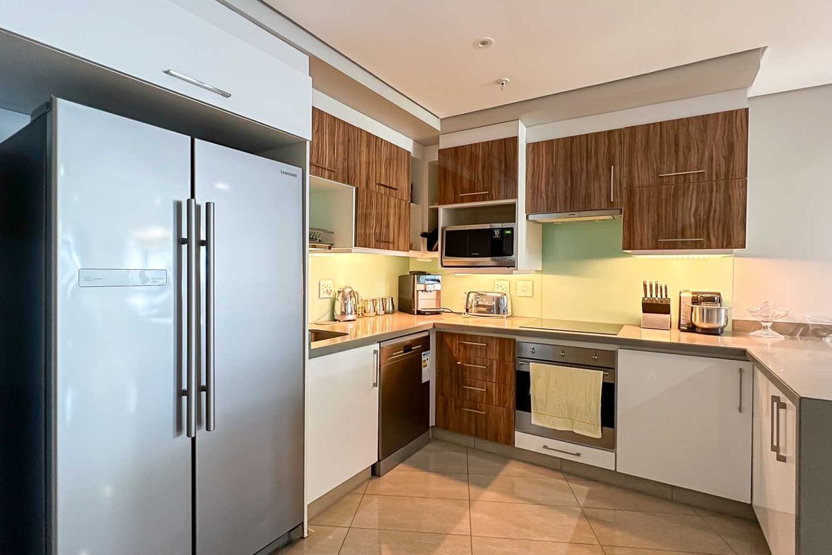 Modern kitchen featuring wood-grain and white cabinetry, stone countertops, integrated appliances, and a glass splashback in a well-lit, functional layout.