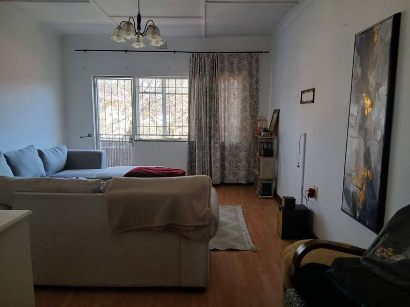 A living room featuring laminate flooring, ceiling panels, and a security gate leading to the exterior.