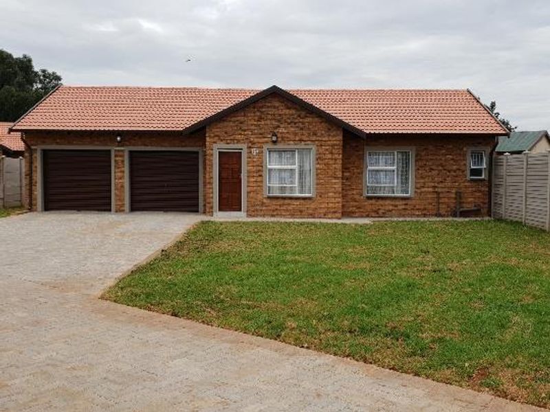Front view of a single-story townhouse featuring a double garage, brick exterior, tiled roof, paved driveway, and a well-maintained front lawn.