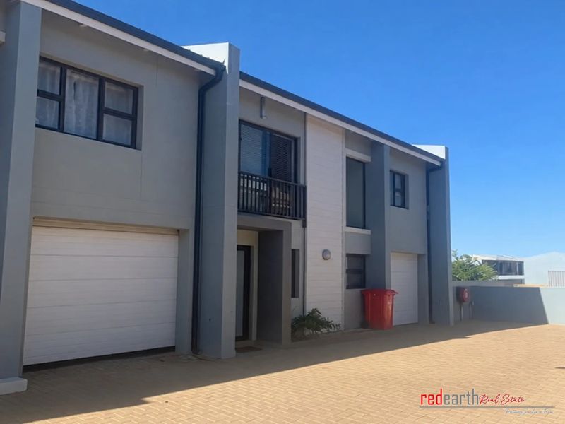 Modern double-storey townhouse exterior featuring a paved driveway, double garage, and a private balcony with contemporary grey and white facade finishes.