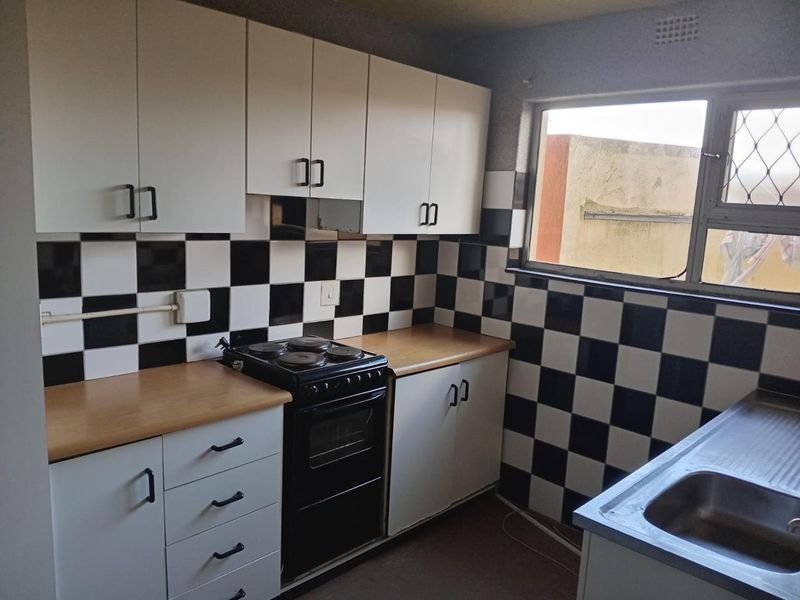 A functional kitchen featuring white cabinetry, black and white checkered tiled backsplash, laminate countertops, and a freestanding stove with a stainless steel sink.