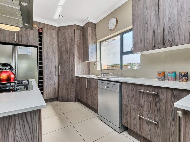 Modern kitchen featuring wood-grain cabinetry, stone countertops, a gas hob with extractor, and integrated dishwasher, finished with neutral floor tiles.