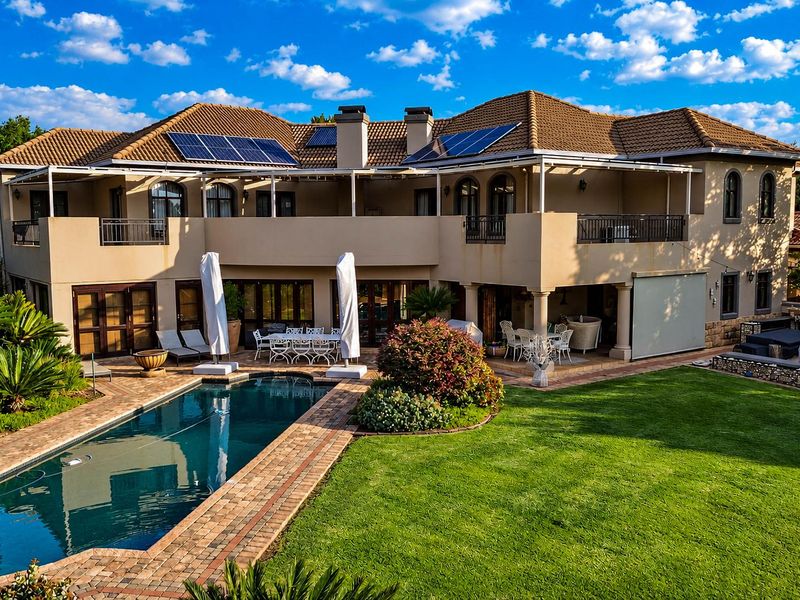 Spacious rear exterior view featuring a large swimming pool, manicured lawn, covered patio, balcony, and solar panels installed on the tiled roof.