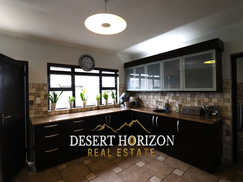 A functional kitchen featuring dark cabinetry, granite countertops, a tiled backsplash, and a double sink, offering ample storage and workspace.