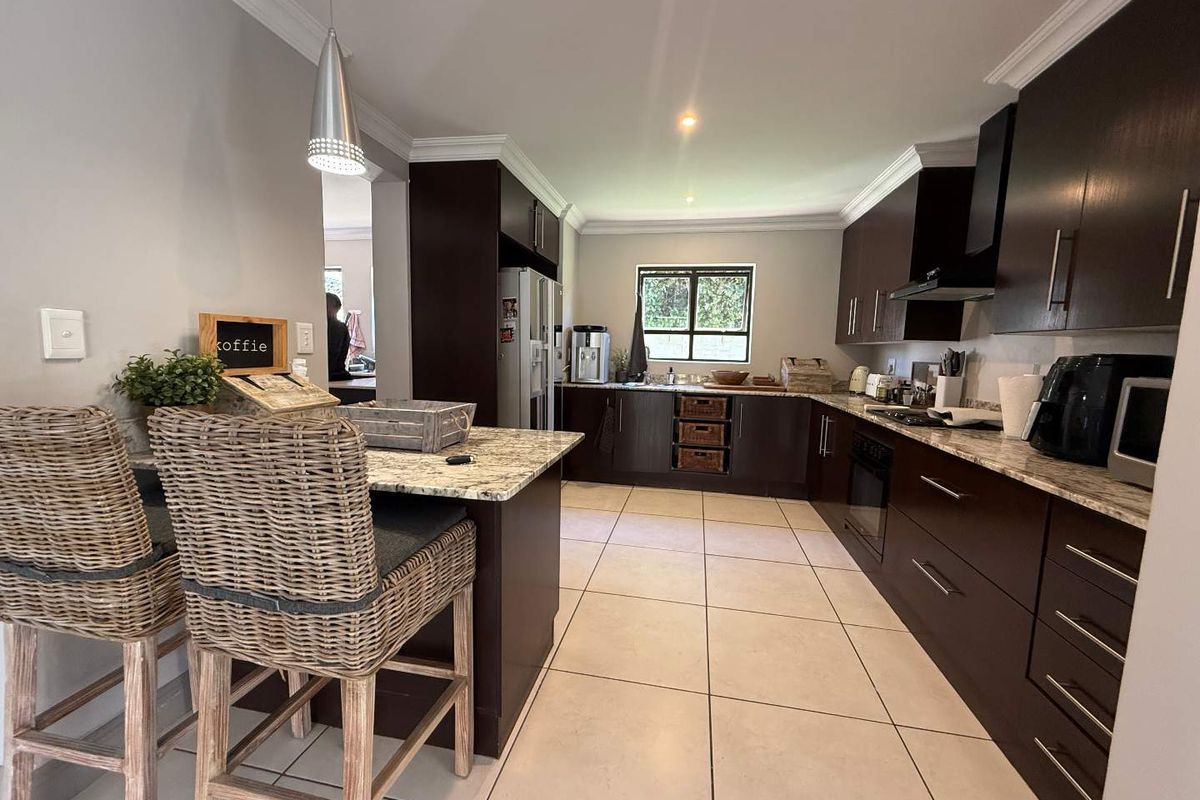 A modern kitchen featuring dark wood cabinetry, granite countertops, a breakfast island, and tiled flooring with recessed lighting.