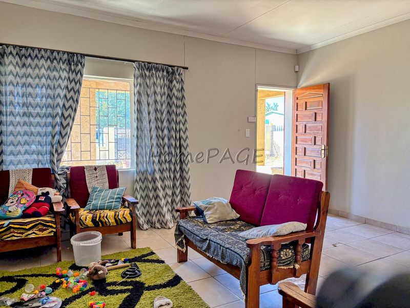 A living room area featuring tiled flooring, a timber entrance door, and window security bars, providing a functional and accessible living space.