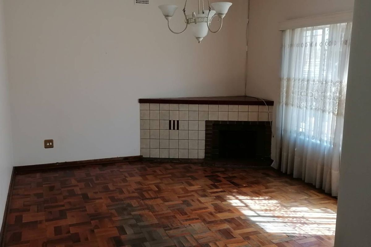 A vacant living room featuring original parquet flooring and a corner fireplace with a tiled surround, offering a blank canvas for renovation.