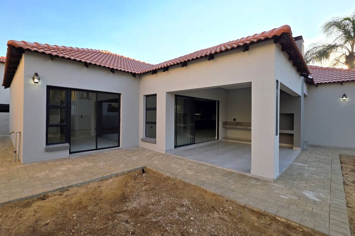Rear view of the property featuring a covered patio with a built-in braai, tiled flooring, and sliding glass doors leading into the home.