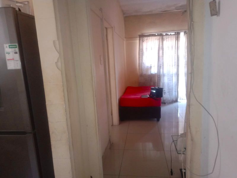 A view from a hallway into a living area featuring tiled floors and a sliding glass door, showing signs of wear and maintenance needs.