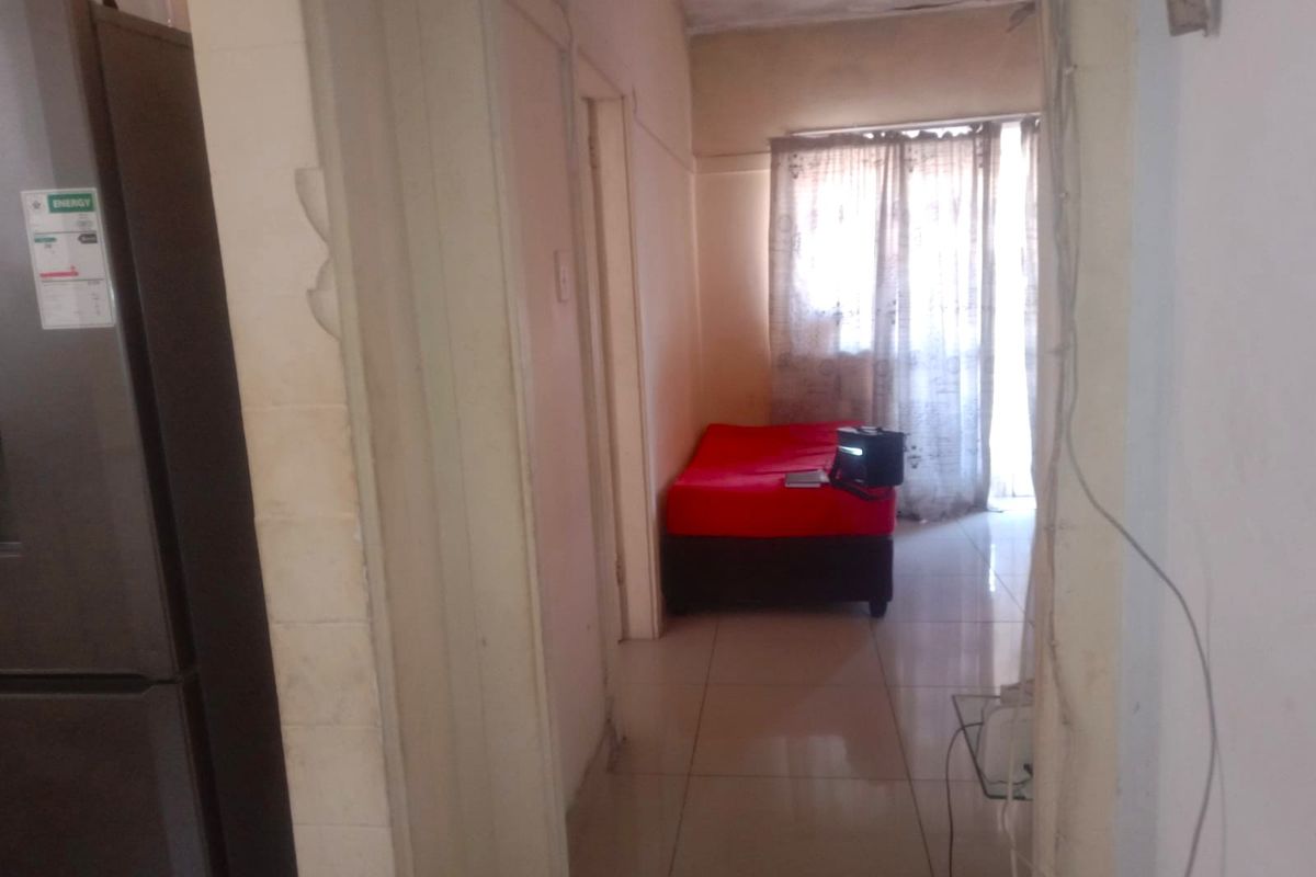 A view from a hallway into a living area featuring tiled floors and a sliding glass door, showing signs of wear and maintenance needs.