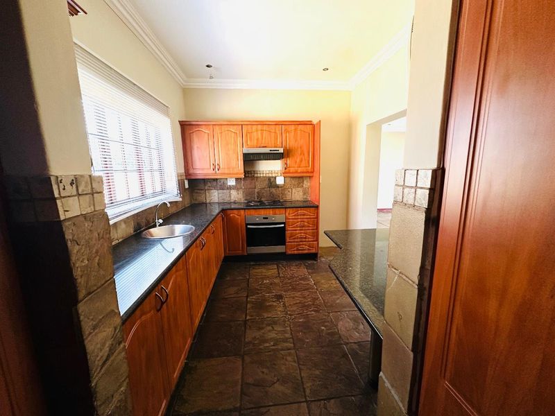 A functional kitchen featuring wooden cabinetry, granite countertops, built-in oven and hob, and tiled flooring, offering a practical layout for meal preparation.
