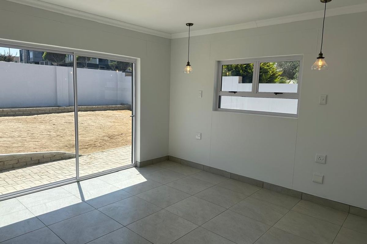 A bright, empty living area featuring large sliding glass doors leading to the backyard, tiled flooring, and modern pendant lighting.