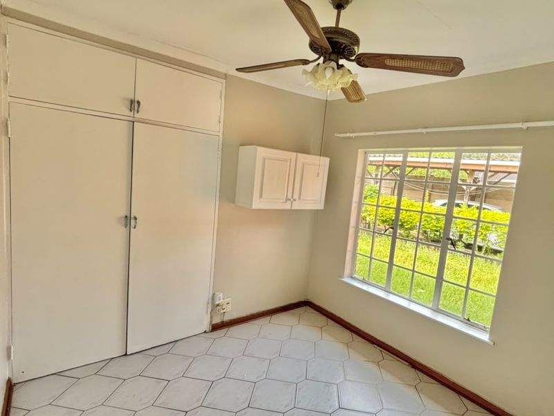 A bright, empty bedroom featuring built-in cupboards, a ceiling fan, and tiled flooring, offering a clean canvas for personalization.