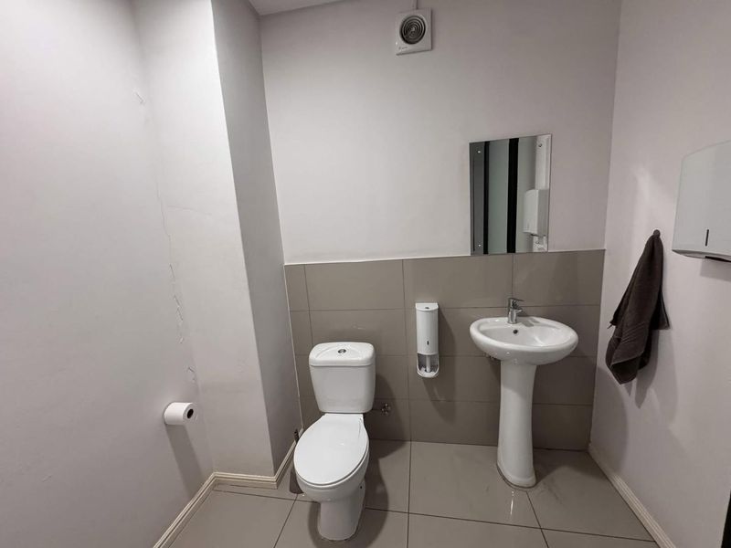 A functional bathroom featuring a pedestal basin, toilet, and tiled finishes, showing visible wall plaster cracking.