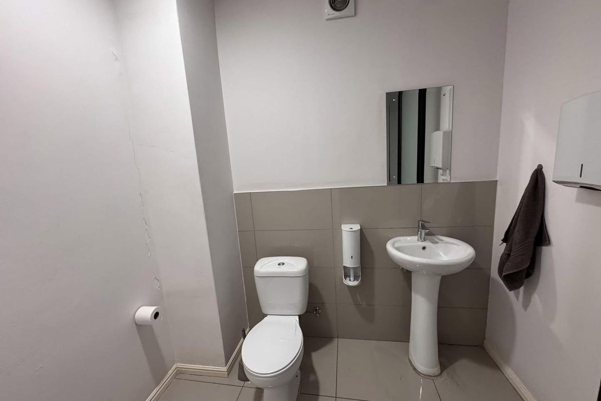 A functional bathroom featuring a pedestal basin, toilet, and tiled finishes, showing visible wall plaster cracking.