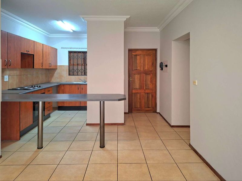 A functional kitchen featuring wooden cabinetry, a breakfast bar, built-in hob and oven, and tiled flooring, offering a practical layout for daily use.