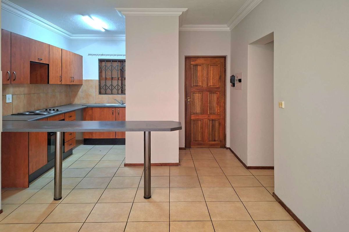 A functional kitchen featuring wooden cabinetry, a breakfast bar, built-in hob and oven, and tiled flooring, offering a practical layout for daily use.