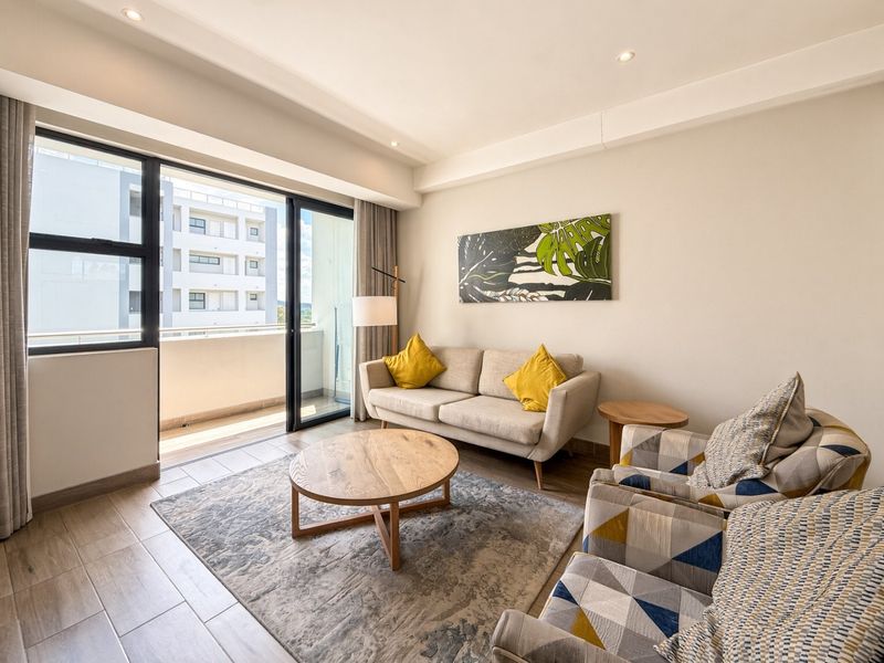 A bright and modern living room featuring tiled flooring, recessed downlighting, and large sliding glass doors that open onto a private balcony.