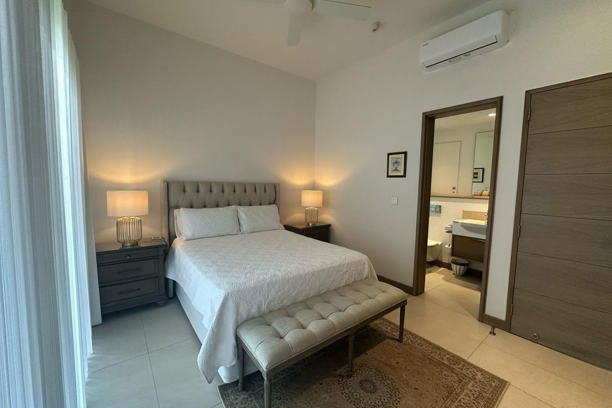 A well-maintained bedroom featuring tiled flooring, a ceiling fan, and a wall-mounted air conditioning unit, with an attached en-suite bathroom.