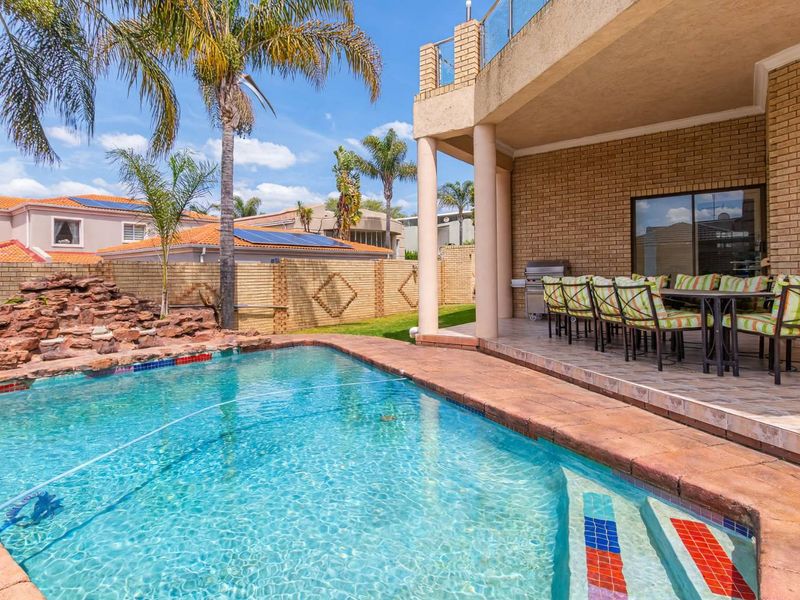 Outdoor entertainment area featuring a swimming pool, rock water feature, and a covered patio with tiled flooring and brick wall finishes.