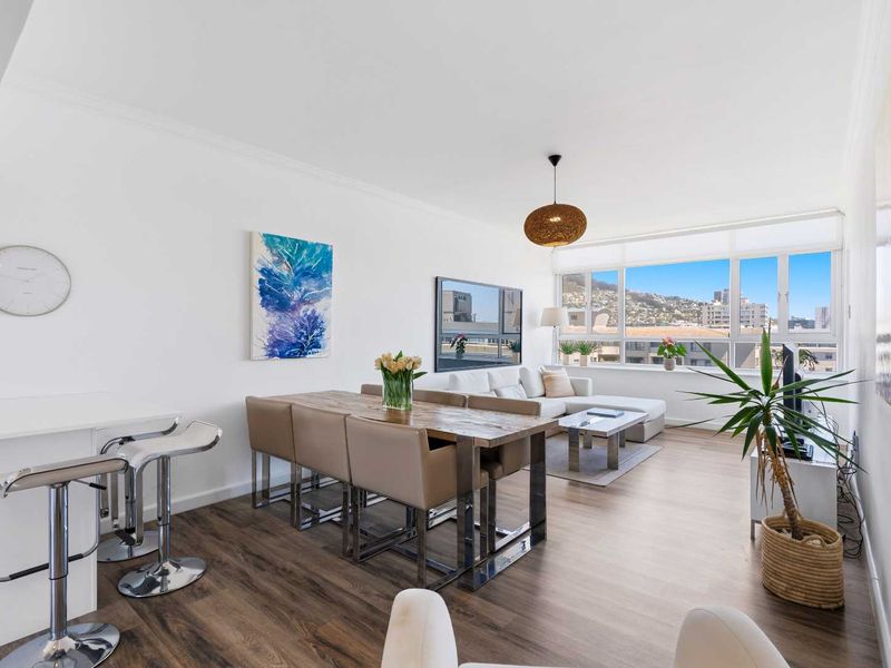 Bright open-plan living and dining area featuring modern laminate flooring, a breakfast counter, and large windows offering expansive urban and mountain views.