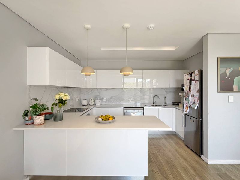 Modern kitchen featuring sleek white cabinetry, marble-look splashback, stone countertops, breakfast bar, and integrated appliances in a clean, contemporary design.