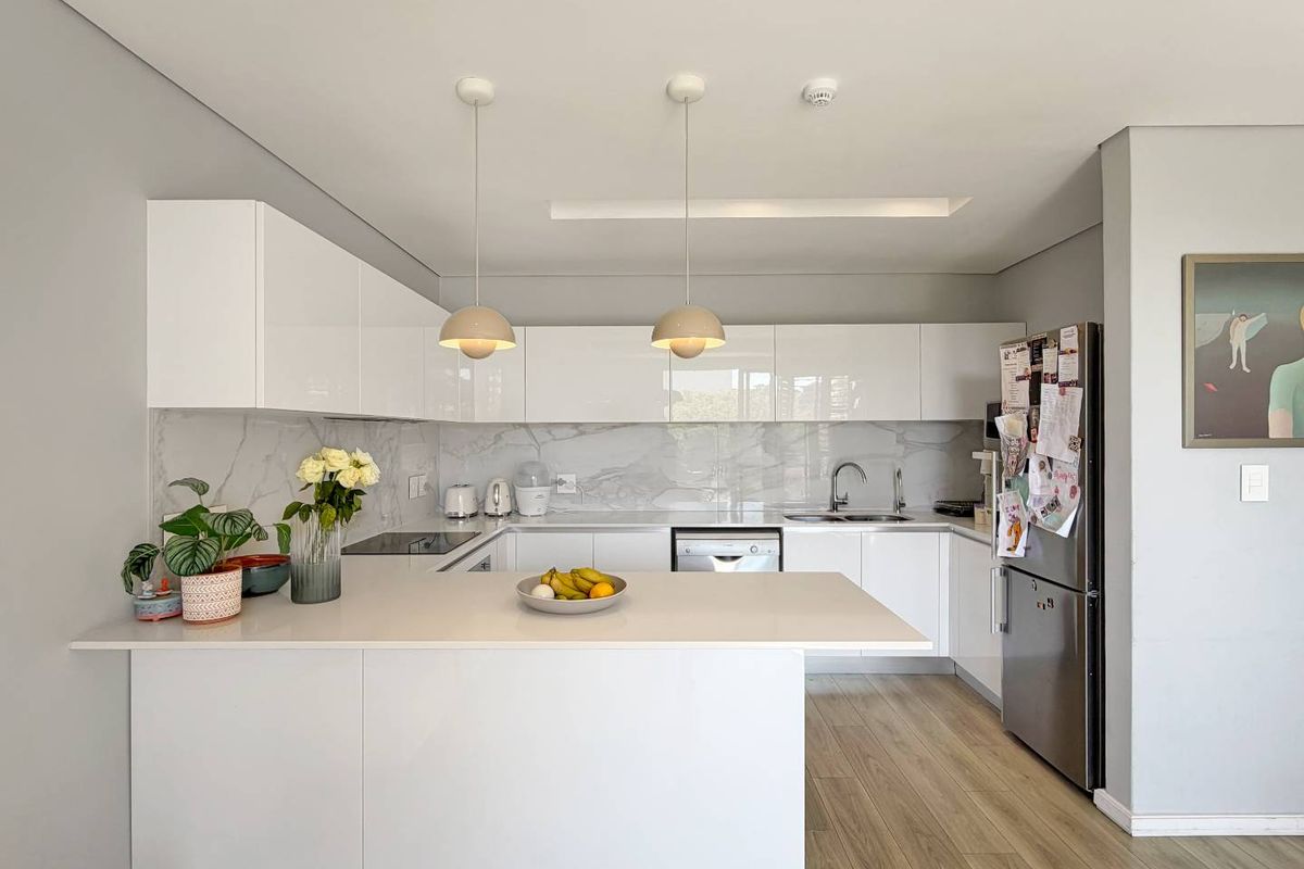 Modern kitchen featuring sleek white cabinetry, marble-look splashback, stone countertops, breakfast bar, and integrated appliances in a clean, contemporary design.