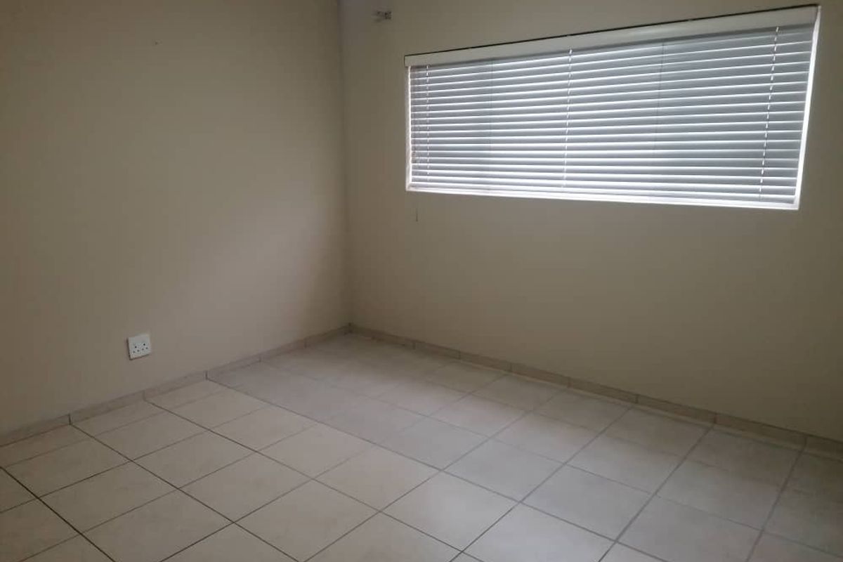 A clean, empty bedroom featuring neutral tiled flooring, painted walls, and fitted horizontal window blinds.
