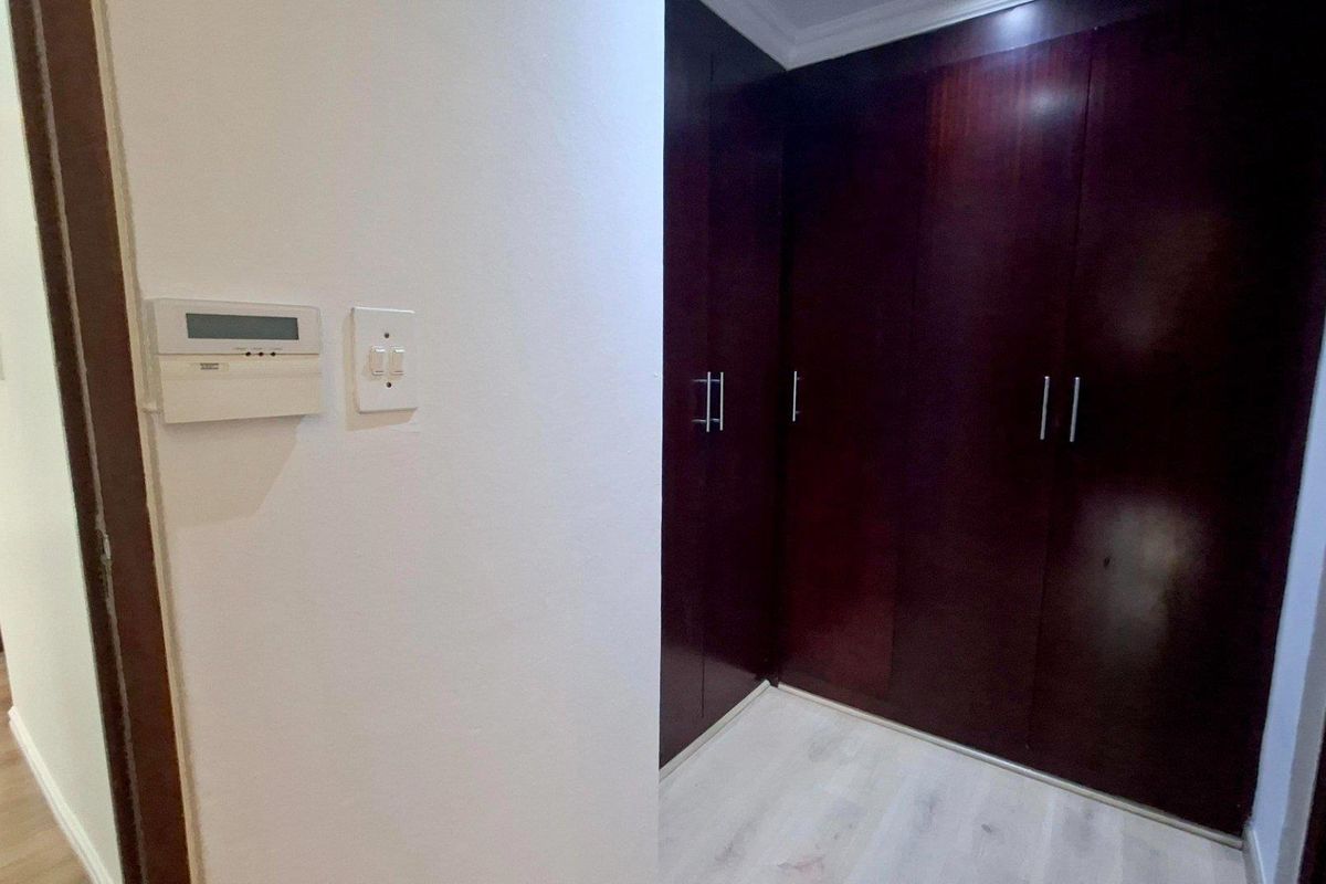 A clean bedroom area featuring dark wood built-in cupboards, light laminate flooring, and a wall-mounted climate control unit.