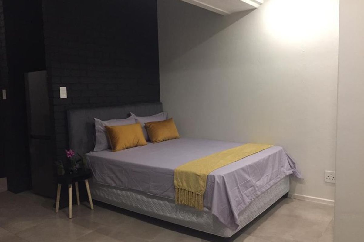 A bedroom featuring a dark exposed brick accent wall, neutral tiled flooring, and modern lighting, providing a clean and contemporary sleeping space.