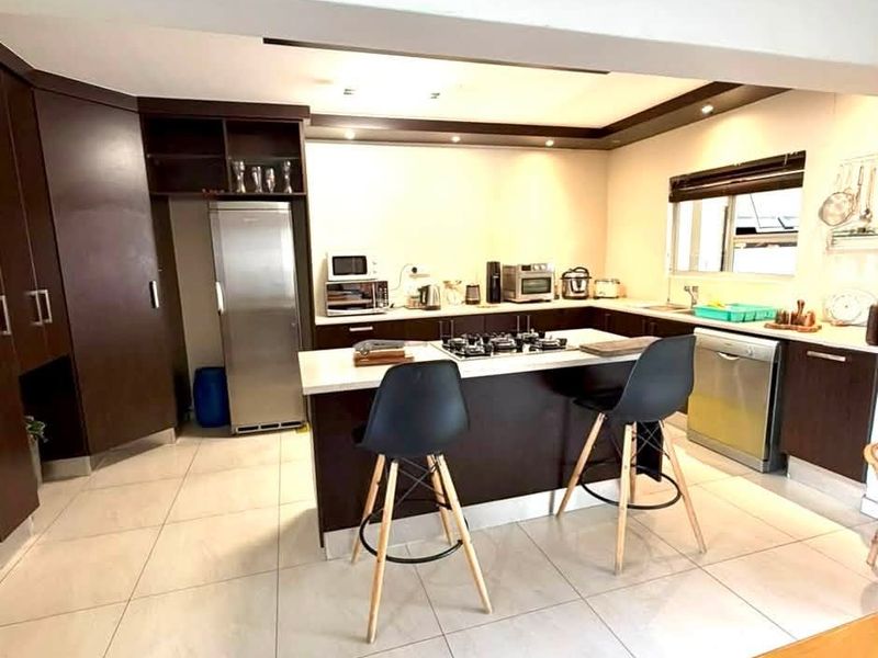 Modern kitchen featuring dark wood cabinetry, a central island with a gas hob, tiled flooring, and recessed lighting.